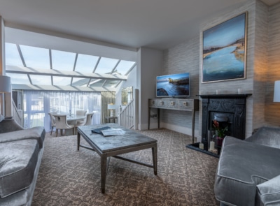 Luxurious hotel suite with a plush bed, elegant furnishings, large windows offering scenic views, a cozy seating area, and modern decor in a warm, inviting color palette.