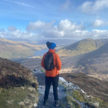 A hiker walks along a scenic trail with lush green hills and cloudy skies at Connemara National Park in County Galway.